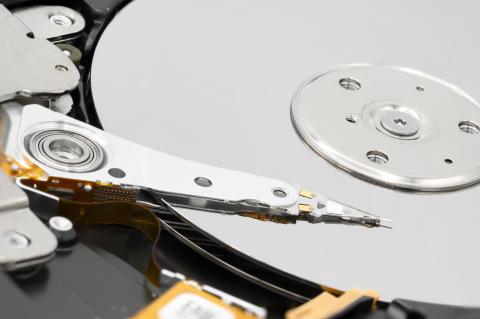 Close-up of a disassembled computer hard disk drive with the magnetic head at the end of the actuator arm, the platter covered with magnetic material and the disk spindle.